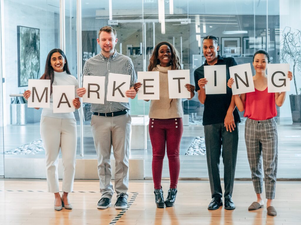 A digital marketing team each holding up a paper spelling the word "Marketing"